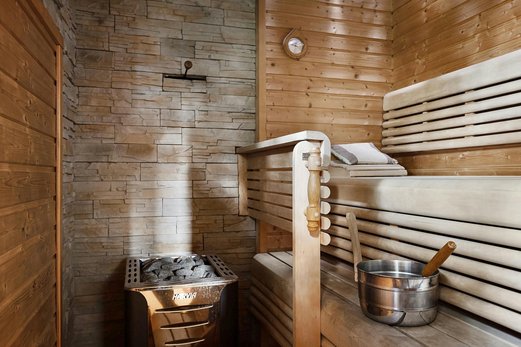 Featuring a relaxing sauna interior with wooden benches and a stone wall heater for a serene escape.